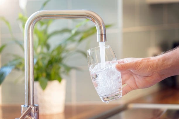 clean water coming from tap where man is filling it on clean glass